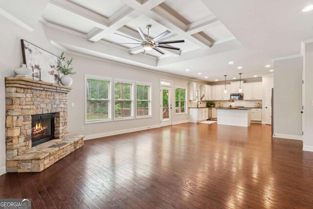 unfurnished living room featuring a ceiling fan, hardwood / wood-style floors, a stone fireplace, beamed ceiling, and ornamental molding