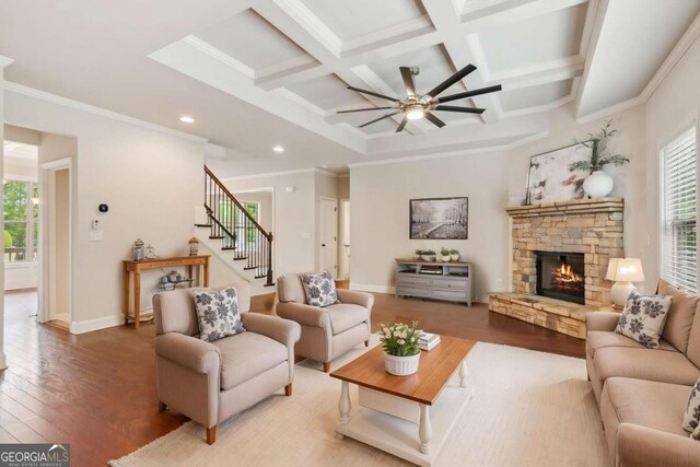 living area with ceiling fan, wood finished floors, a stone fireplace, beam ceiling, and stairway