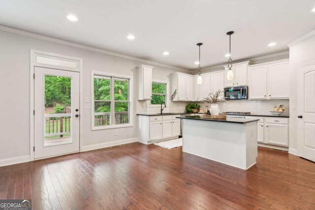 kitchen featuring stainless steel microwave, dark countertops, ornamental molding, decorative backsplash, and white cabinetry