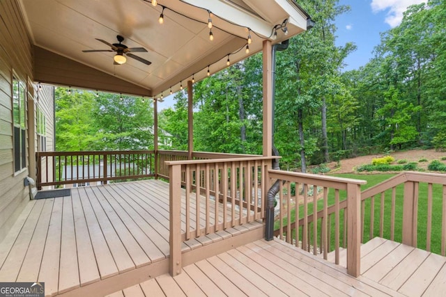 deck with a ceiling fan, view of scattered trees, and a lawn