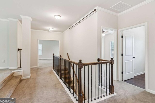 corridor featuring an upstairs landing, ornamental molding, carpet, and baseboards