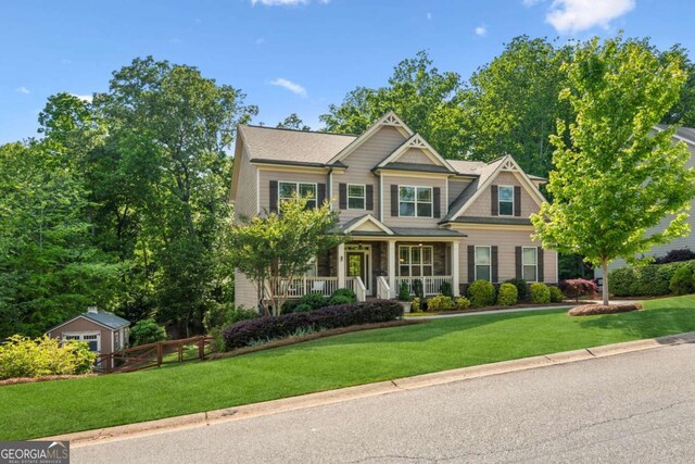 craftsman-style home featuring covered porch, a front yard, and an outbuilding