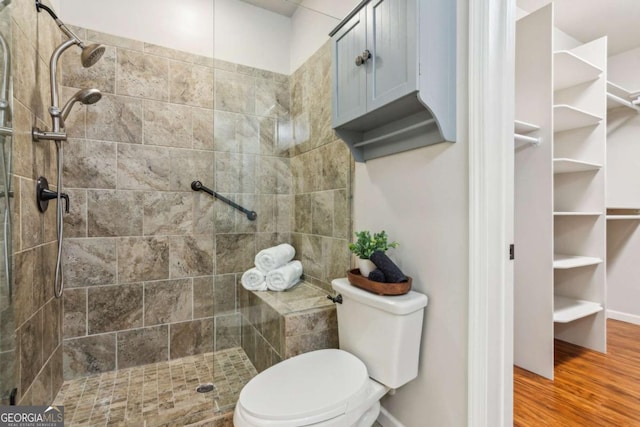 bathroom featuring a tile shower, wood finished floors, and toilet