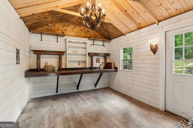 interior space featuring wood walls, vaulted ceiling, a chandelier, healthy amount of natural light, and wood finished floors