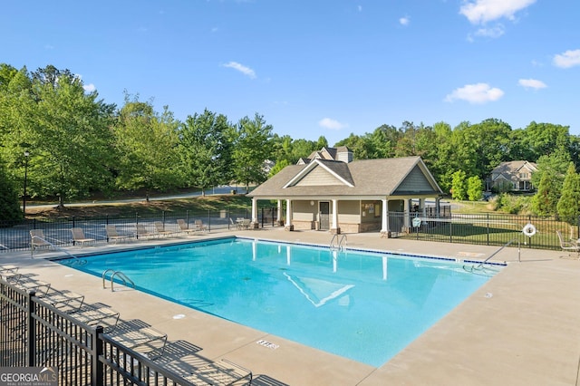 community pool with fence, a patio, and view of wooded area