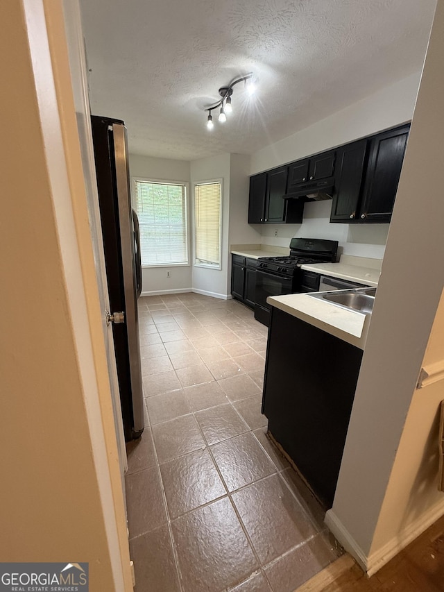 6449 Pinebark Way, Morrow, GA 30260 - kitchen featuring dark cabinetry, black gas stove, freestanding refrigerator, a sink, and a textured ceiling