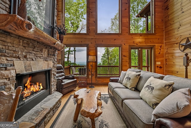 living room with a towering ceiling, a fireplace, wooden walls, and wood finished floors