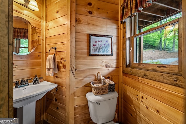 half bathroom featuring wooden walls, toilet, plenty of natural light, and a sink
