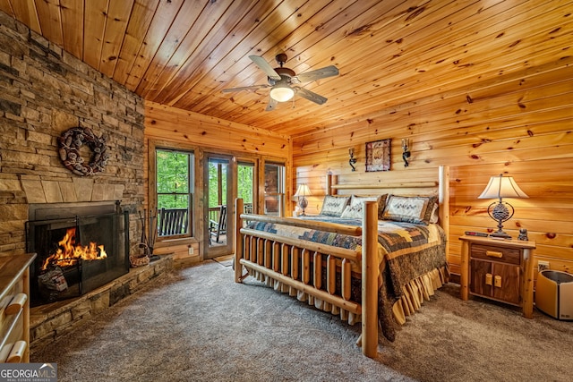 carpeted bedroom featuring access to exterior, wooden ceiling, a stone fireplace, and wood walls