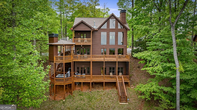 back of property with a chimney, a balcony, stairs, a wooden deck, and a shingled roof