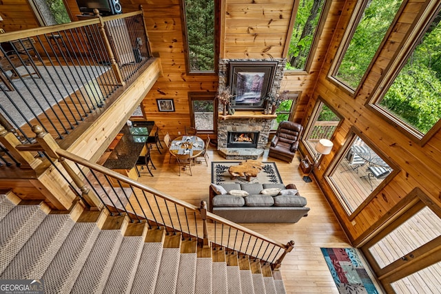 living room featuring plenty of natural light, wood walls, hardwood / wood-style flooring, a fireplace, and stairway
