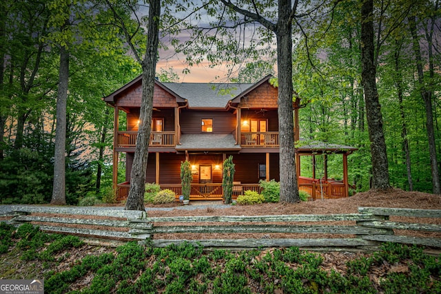 rear view of property with a balcony, covered porch, and a shingled roof