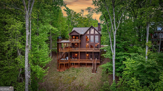 back of house at dusk with a balcony, a chimney, stairs, and a deck