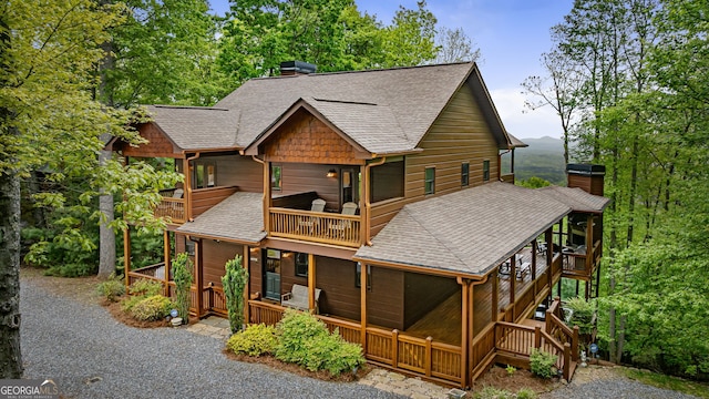 rear view of property featuring a chimney, a balcony, and roof with shingles