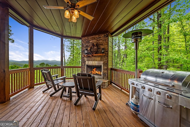 wooden terrace featuring an outdoor stone fireplace, a mountain view, and a ceiling fan