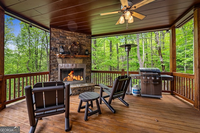 wooden deck with a grill, an outdoor stone fireplace, a ceiling fan, and a forest view