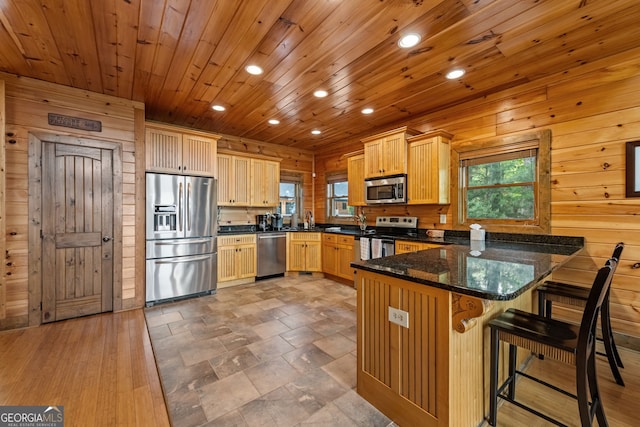 kitchen with stainless steel appliances, a peninsula, recessed lighting, wood walls, and light brown cabinetry