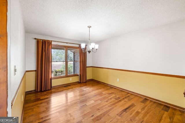 empty room with a chandelier, light wood-style flooring, a textured ceiling, and baseboards
