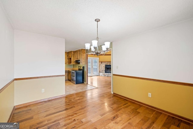 unfurnished dining area with a chandelier, light wood-style floors, baseboards, a fireplace with raised hearth, and a textured ceiling