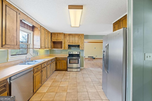 kitchen featuring stainless steel appliances, a sink, exhaust hood, light countertops, and a textured ceiling