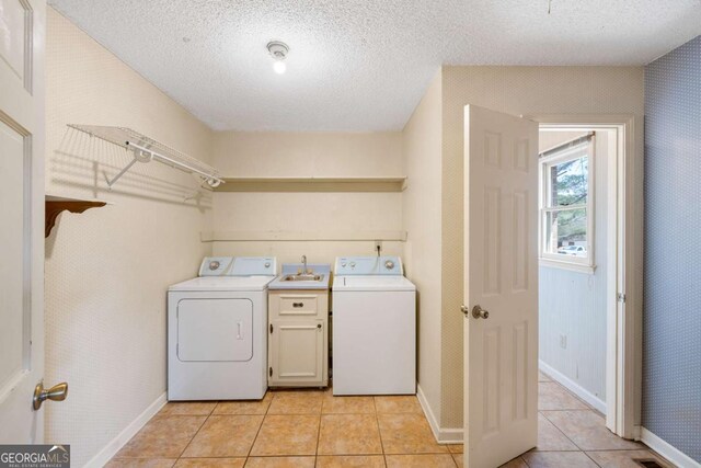 clothes washing area with light tile patterned floors, a textured ceiling, baseboards, a sink, and separate washer and dryer