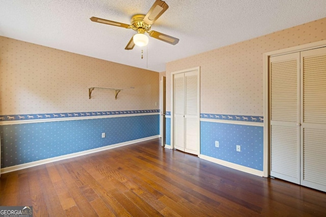 unfurnished bedroom with wallpapered walls, wood finished floors, baseboards, two closets, and a textured ceiling