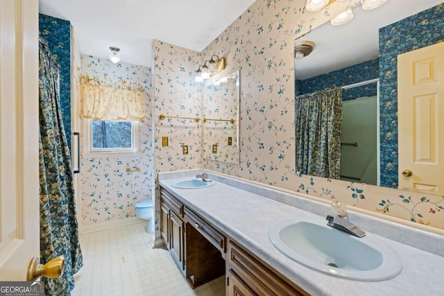 bathroom featuring wallpapered walls, toilet, double vanity, a shower with curtain, and baseboards