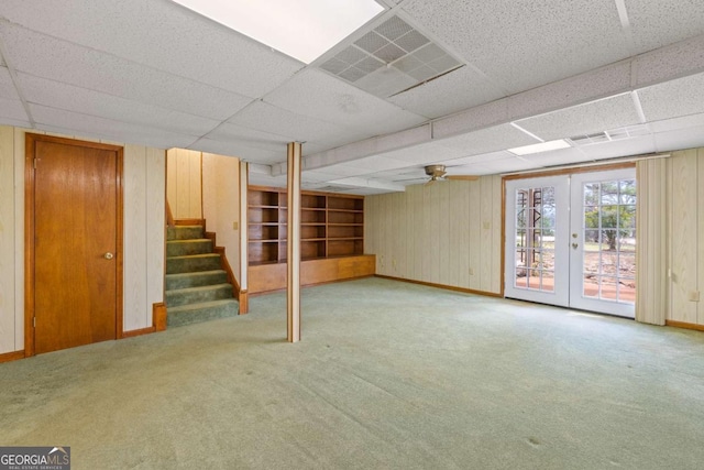 basement with a drop ceiling, light colored carpet, french doors, stairs, and baseboards