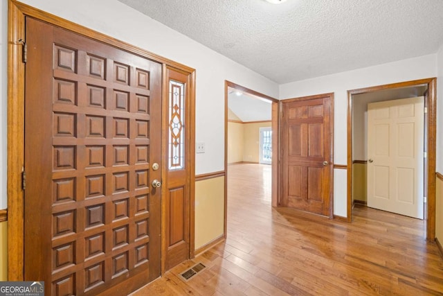 foyer with a textured ceiling, light wood-type flooring, and baseboards