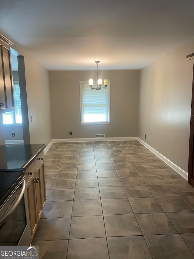 unfurnished dining area with dark tile patterned flooring, plenty of natural light, a chandelier, and baseboards