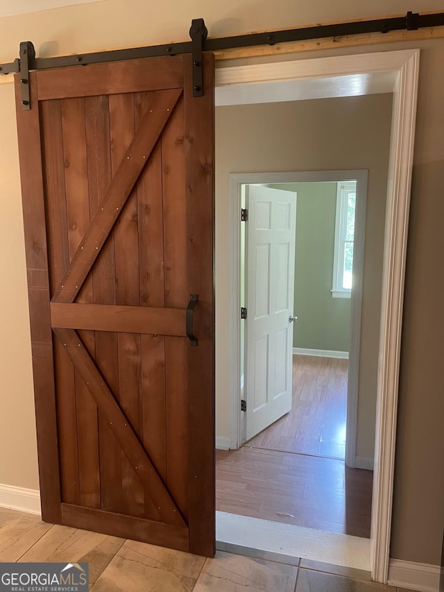 hall with a barn door, light wood-style floors, and baseboards