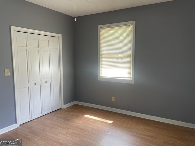 unfurnished bedroom with multiple windows, light wood-type flooring, a closet, baseboards, and a textured ceiling
