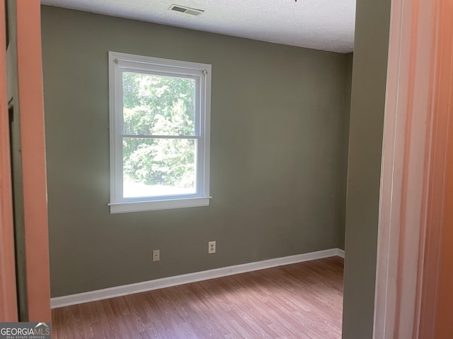 unfurnished room featuring healthy amount of natural light, wood finished floors, baseboards, and a textured ceiling