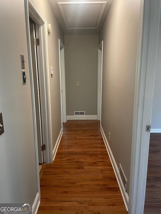 corridor featuring attic access, dark wood-style floors, and baseboards