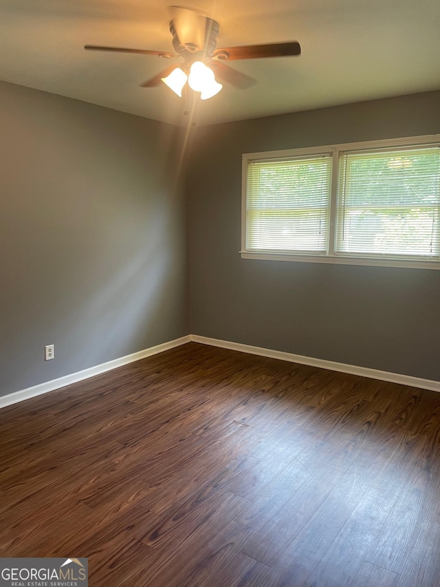 spare room featuring ceiling fan, baseboards, and dark wood-type flooring