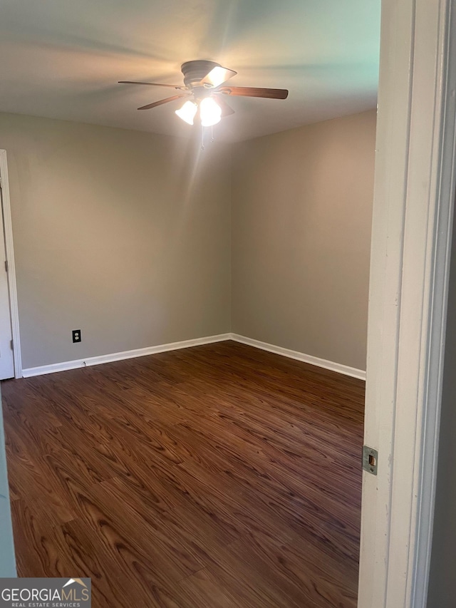 empty room featuring a ceiling fan, dark wood-type flooring, and baseboards