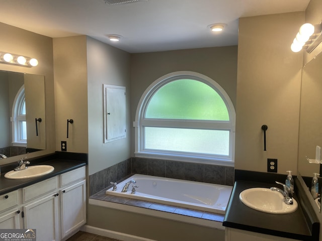 bathroom featuring plenty of natural light, a bath, and two vanities
