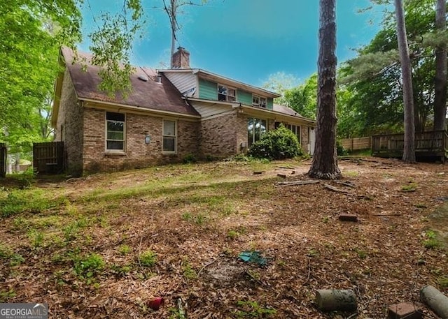 back of property with brick siding, fence, and a chimney