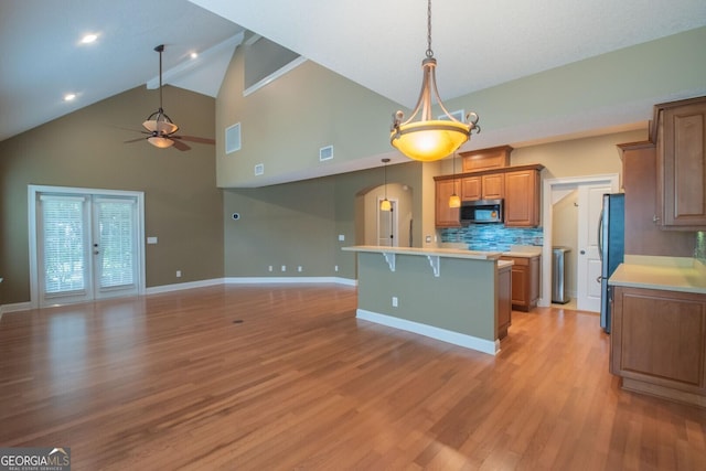 kitchen featuring stainless steel appliances, open floor plan, a ceiling fan, brown cabinetry, and high vaulted ceiling