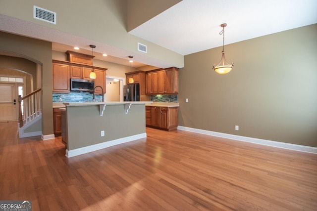 kitchen with stainless steel appliances, brown cabinetry, light wood-type flooring, and a kitchen bar