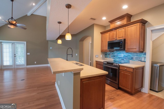 kitchen featuring stainless steel appliances, a sink, arched walkways, a ceiling fan, and light wood-type flooring