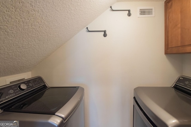laundry area featuring cabinet space, a textured ceiling, and washer and clothes dryer