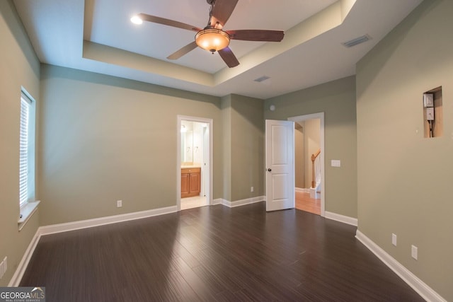 empty room featuring a tray ceiling, ceiling fan, dark wood-style flooring, and baseboards