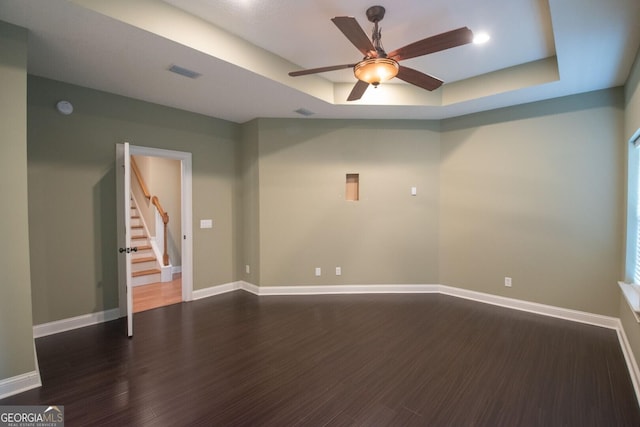 empty room with wood finished floors, stairs, a tray ceiling, and baseboards