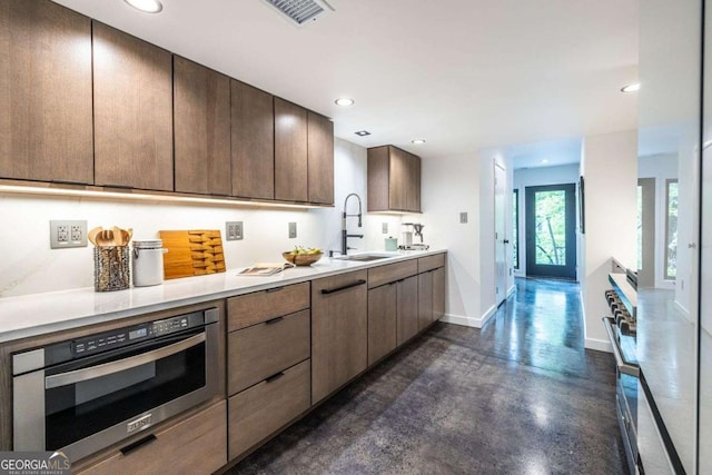 kitchen featuring a sink, stainless steel oven, finished concrete floors, baseboards, and light countertops