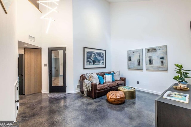 living room featuring a towering ceiling, baseboards, and finished concrete flooring