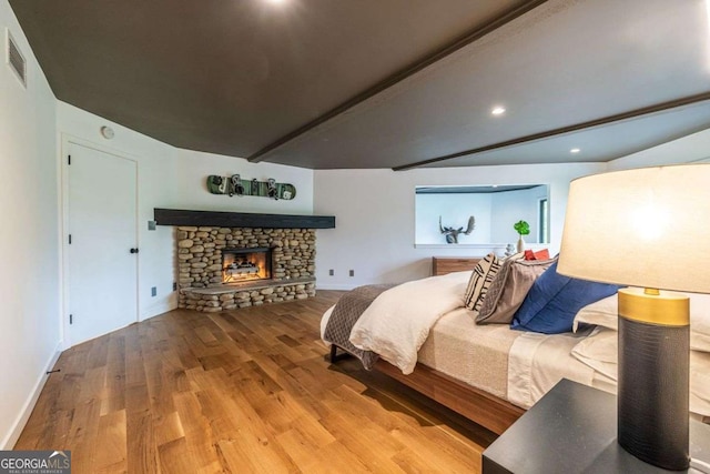bedroom with wood finished floors, beamed ceiling, a fireplace, baseboards, and recessed lighting
