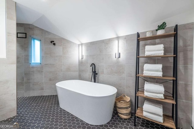 full bathroom with a freestanding bath, tile walls, lofted ceiling, tiled shower, and tile patterned floors