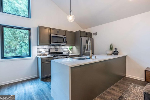 kitchen with appliances with stainless steel finishes, high vaulted ceiling, a peninsula, dark wood-type flooring, and light countertops