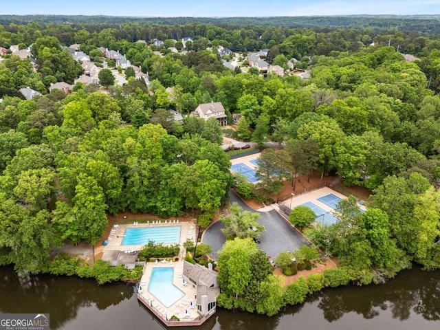 aerial view of a pool, a nearby body of water, and a heavily wooded area